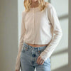 Woman wearing a beige long-sleeve shirt and blue jeans against a white background