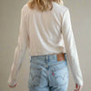 Person wearing a beige long-sleeve top and light blue jeans against a white background
