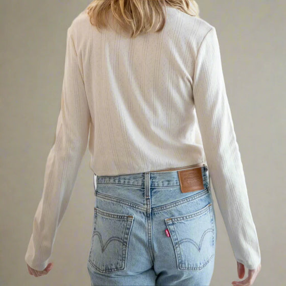 Person wearing a beige long-sleeve top and light blue jeans against a white background
