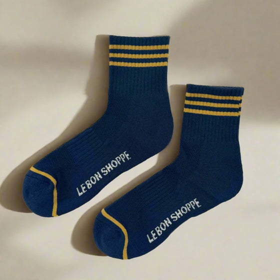 Pair of navy socks with gold stripes and 'Le Bon Shoppe' branding on a white background