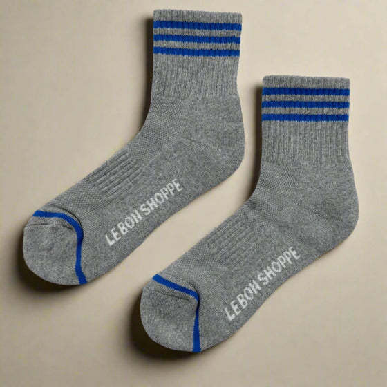 Gray socks with blue stripes and 'Le Bon Shoppe' branding on a light gray background