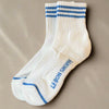 White socks with blue stripes and 'Le Bon Shoppe' branding on a gray surface