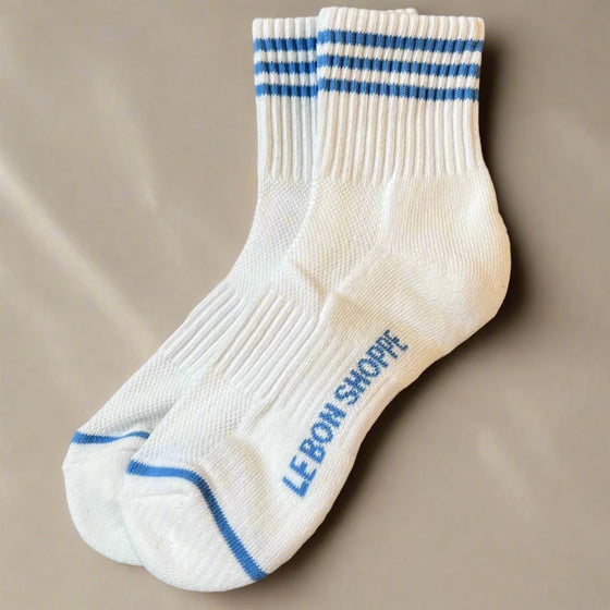 White socks with blue stripes and 'Le Bon Shoppe' branding on a gray surface